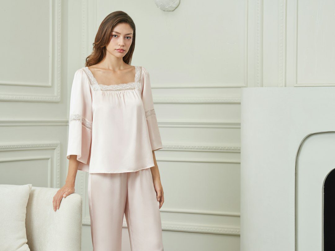 Vrouw in een roze zijden pyjama met kanten rand in een lichte kamer
